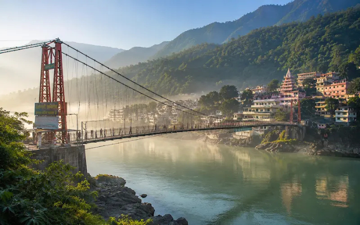 Ram Jhula suspension bridge over the Ganges River in Rishikesh with Himalayan foothills and temples.