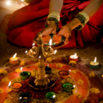 Woman performing diya puja during Dev Diwali in Varanasi 2026 with colorful rangoli and illuminated oil lamps.