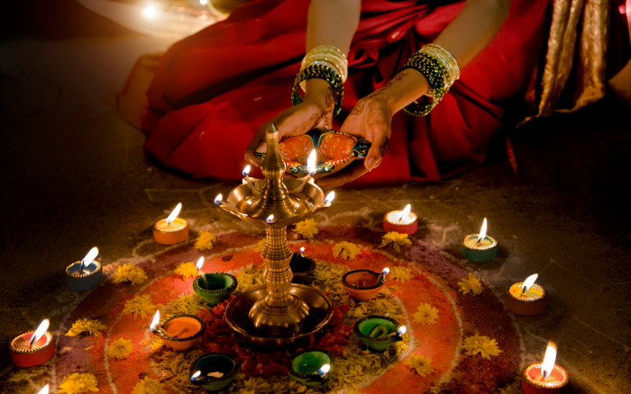 Woman performing diya puja during Dev Diwali in Varanasi 2026 with colorful rangoli and illuminated oil lamps.