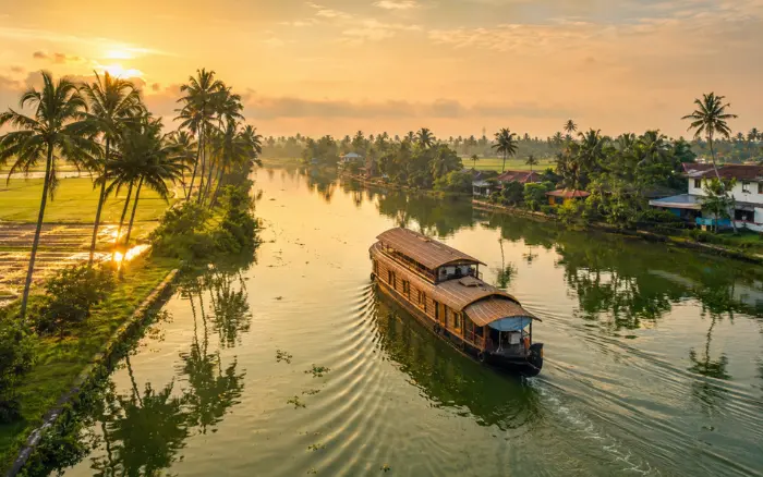 Kerala Backwaters Tour featuring a traditional houseboat cruising through the scenic backwaters of Alleppey, Kerala, surrounded by coconut palms and peaceful waterways.