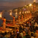 Seven priests in saffron robes performing the synchronized Ganga Aarti fire ceremony at Dashashwamedh Ghat in Varanasi, with large crowds watching from the stone steps beside the Ganges River at dusk